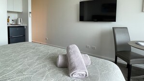 A hotel room with a bed, a television mounted on the wall, a small kitchenette, and a chair. - Coastal Cove Suite with balcony - close to hot springs. (Fingal)