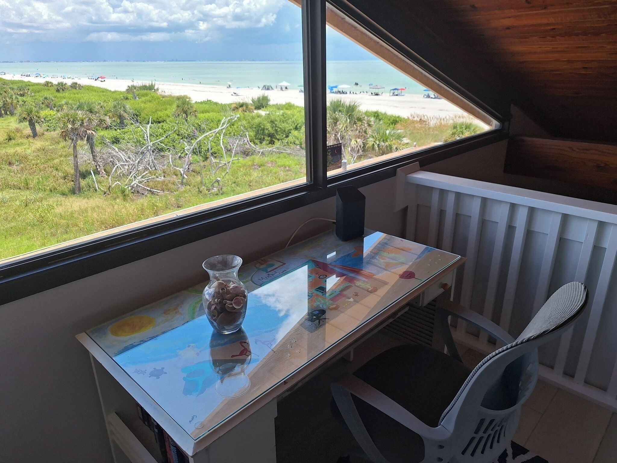 Une pièce avec vue sur la plage, une petite table avec un vase et une chaise blanche.