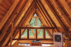 Ein Dachzimmer aus Holz mit schrägem Dach, einem Fenster und einem Heizkörper.