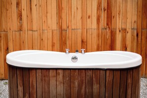 Un bain à remous autonome, doté de deux robinets et d’un drain, installé devant un décor en bois.