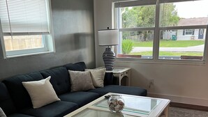 A living room with a dark-colored sofa, a glass-top coffee table, and a lamp on a small table.