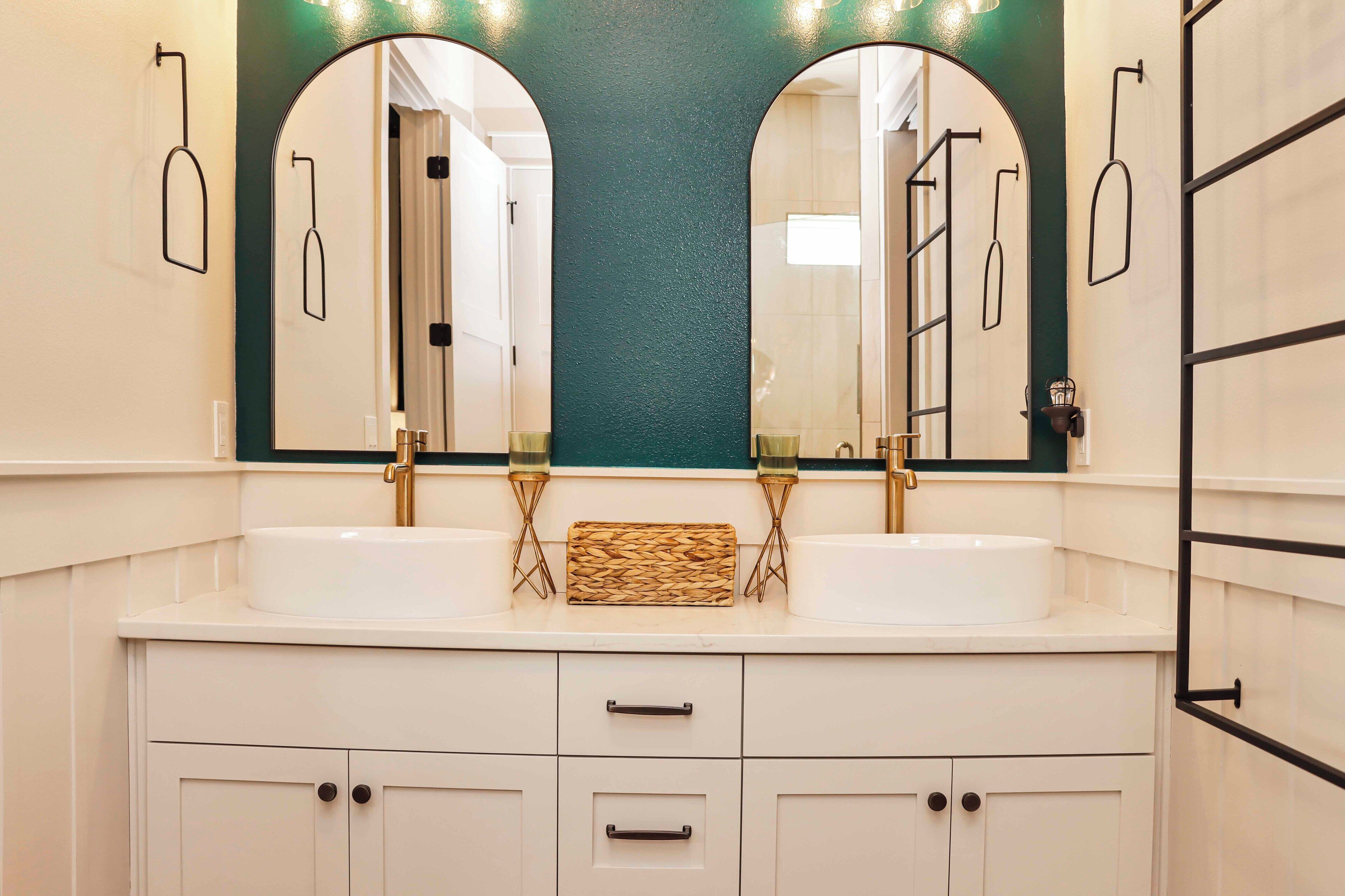 A bathroom with two sinks, a large mirror, and a woven basket between them.