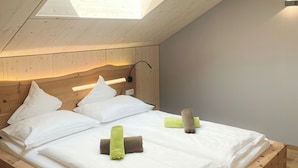 A high-ceilinged room with a skylight, wooden bed frame, white bedding, and a headboard with integrated lighting. - Apartment Schwarzhorn (Barbian)