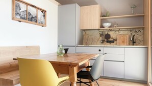 A modern kitchen with wooden cabinets, a marble backsplash, and a dining area with a wooden table and yellow chairs. - Apartment Schwarzhorn (Barbian)