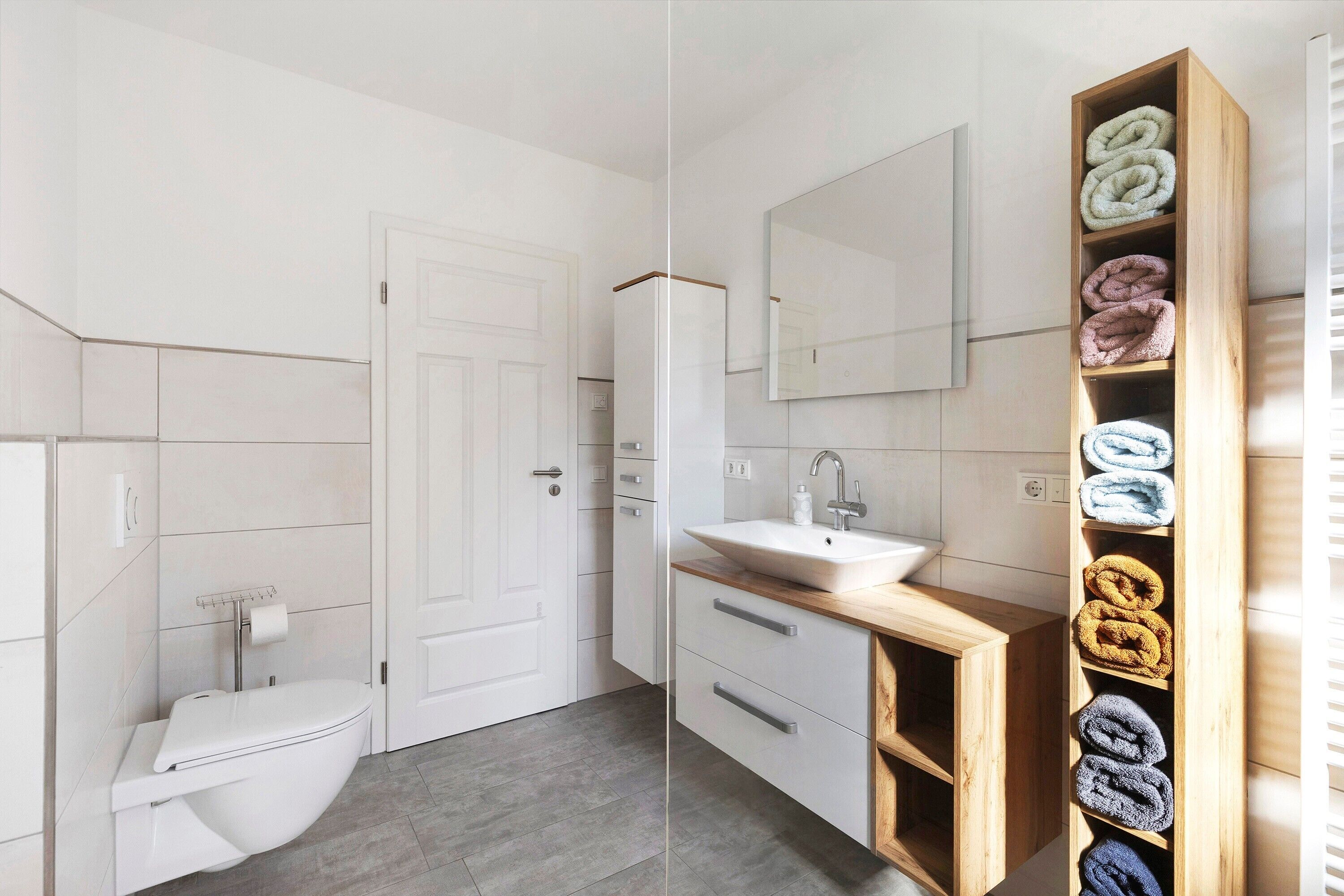 A modern bathroom with a toilet, sink, and wooden towel shelf.
