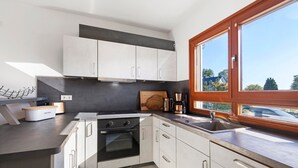 Une cuisine moderne avec des armoires blanches, un four encastré, un évier et une fenêtre donnant sur l’extérieur.