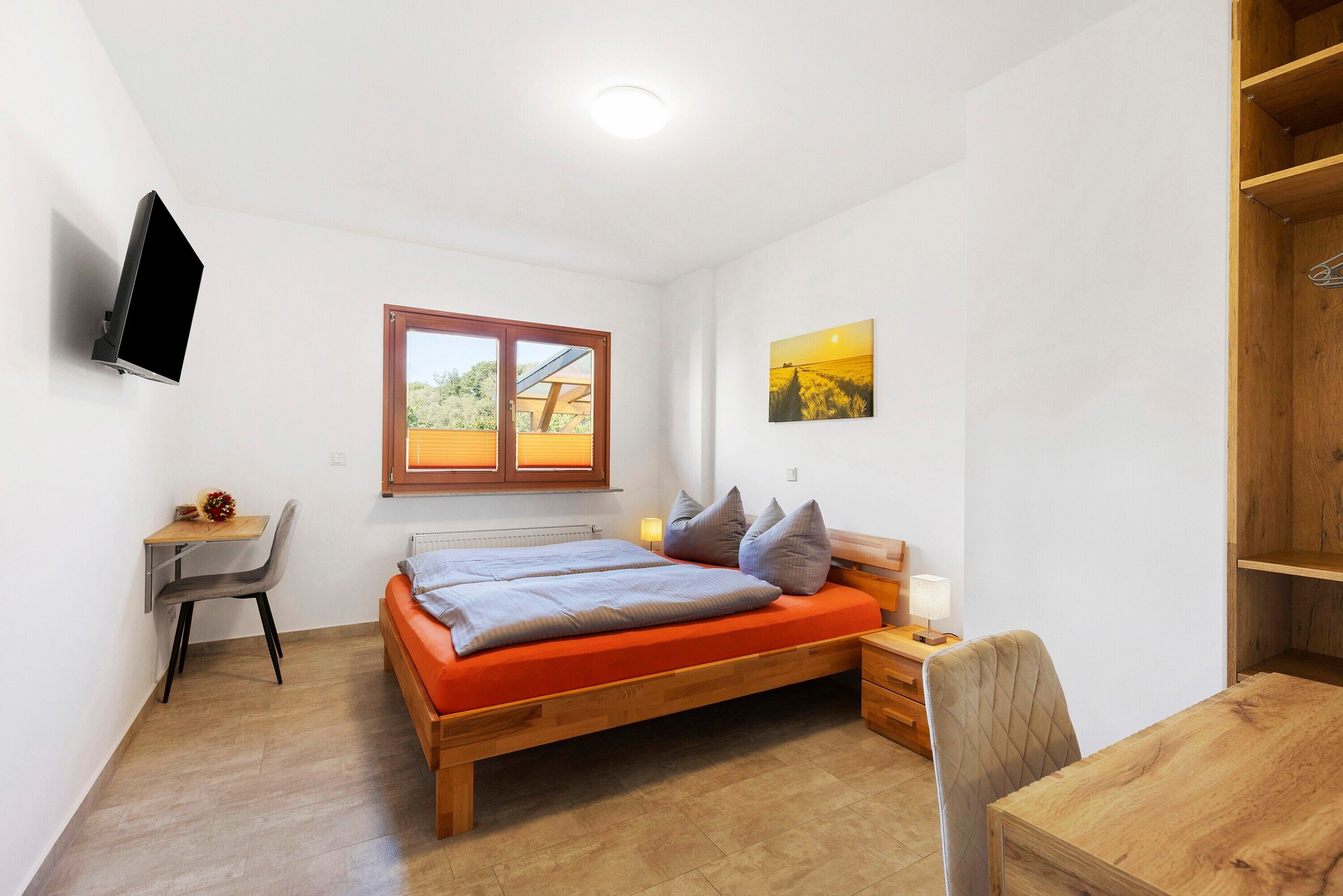 Een slaapkamer met een bed, bureau, stoel en een televisie aan de muur.