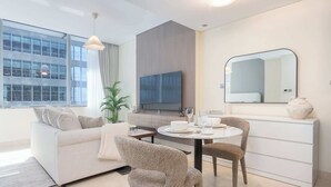 A modern living room with a sofa, two armchairs, a dining table set for two, a TV, a mirror, and a potted plant. - 1209 Sky Gardens in Dubai (Dubai)