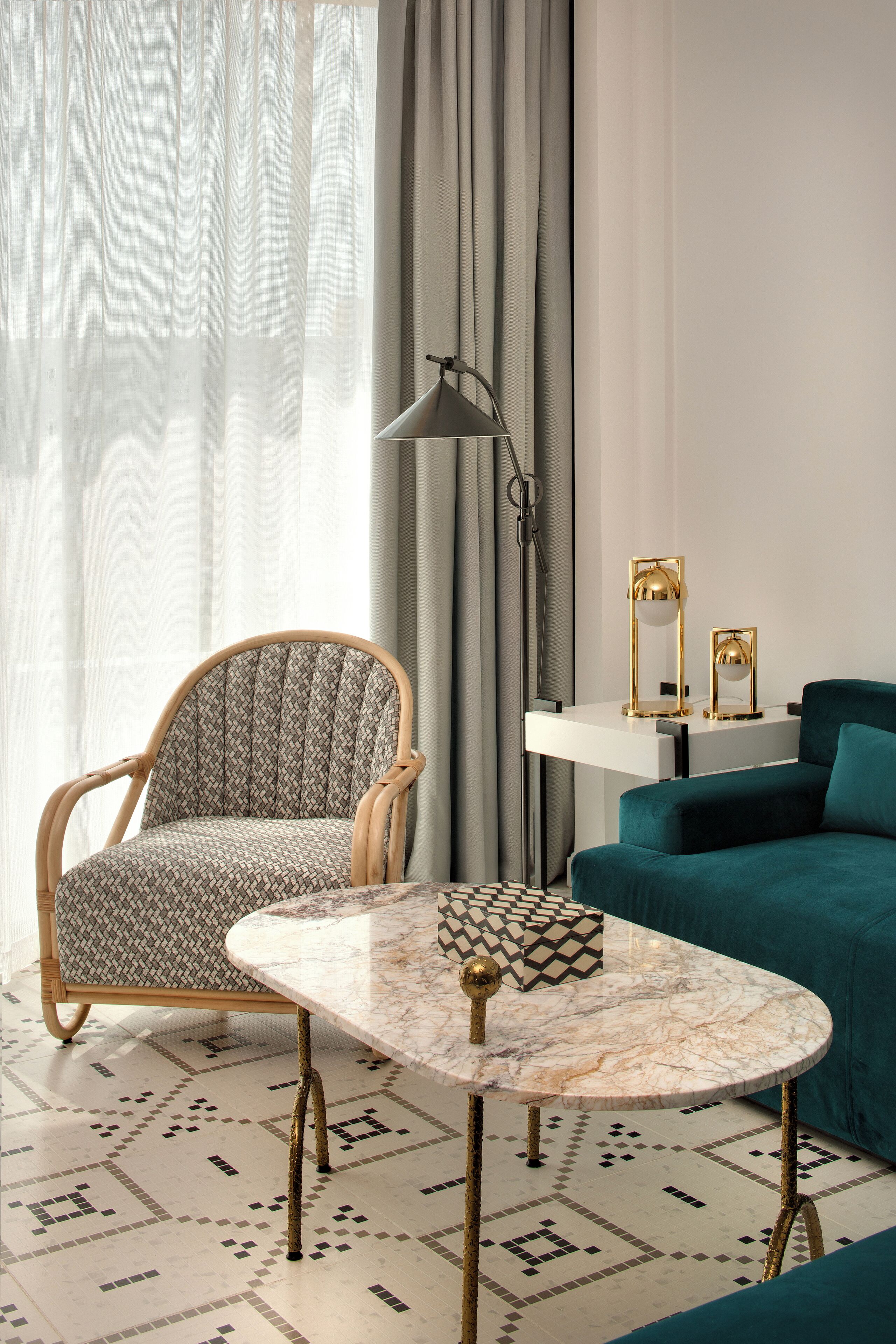 Un salon moderne avec un fauteuil à motifs, un canapé de couleur turquoise, une table basse en marbre et un sol orné de carreaux aux motifs géométriques.
