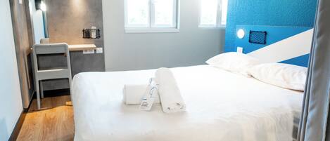 A hotel room with a bed, a desk, a chair, a mirror, and a window.