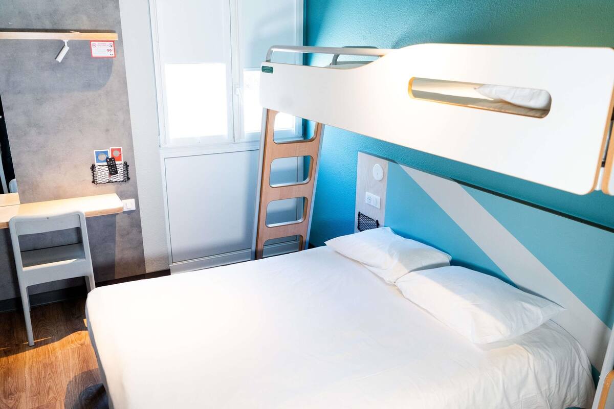 Ein Stockbett mit Schreibtisch und Leiter, ein Fenster und eine Wandsteckdose.