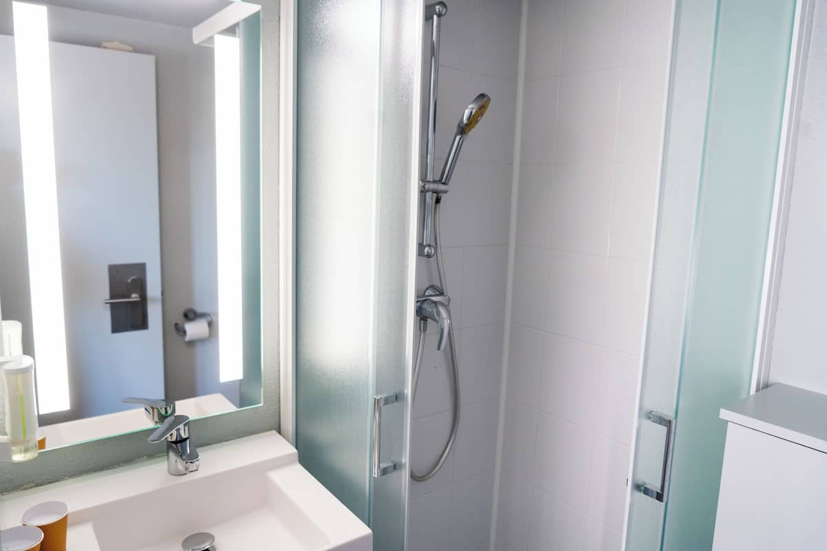 Ein Badezimmer mit einem weißen Waschbecken, einem großen Spiegel und einer Duschkabine mit Glastür.