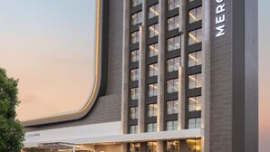 Un hôtel moderne à la façade incurvée, doté de plusieurs étages et d’une entrée imposante avec des portes en verre.