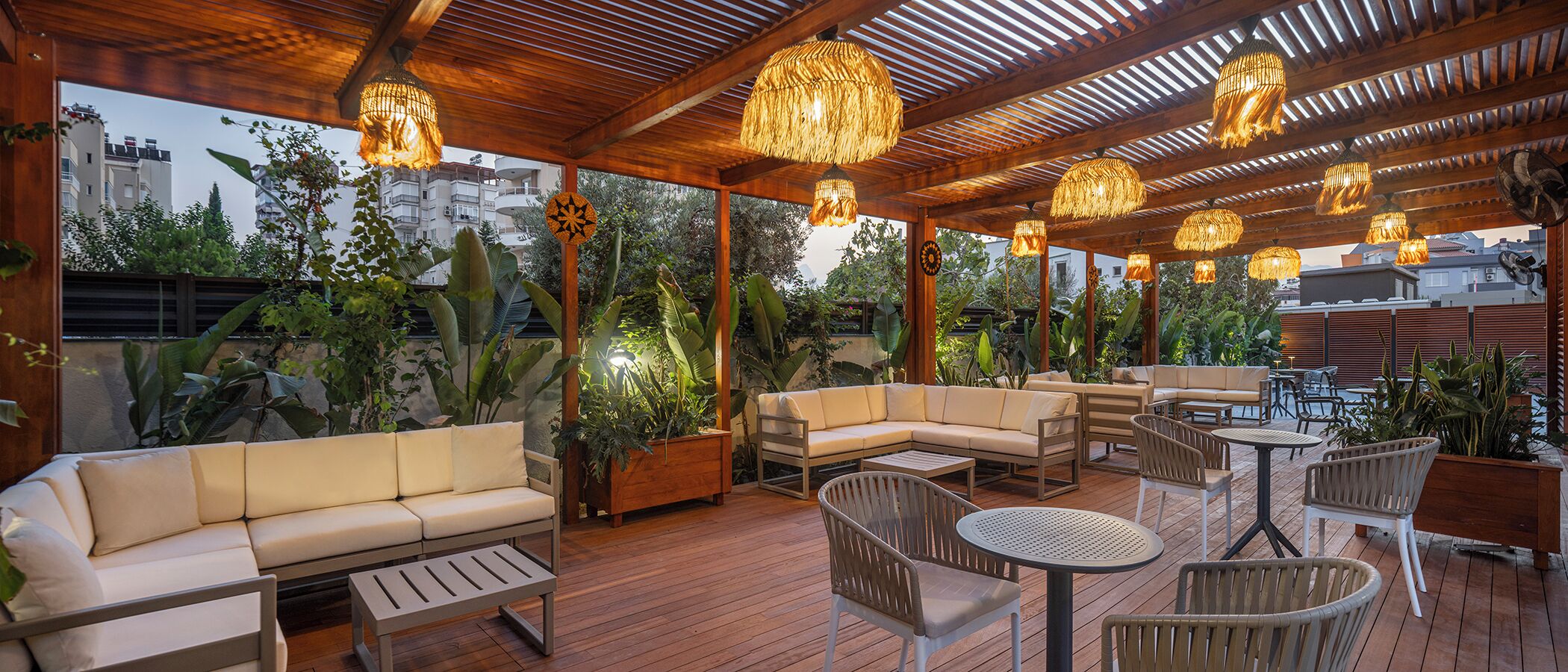 Une terrasse extérieure dotée d’un plancher en bois, de sièges confortables et de lampes en osier suspendues.