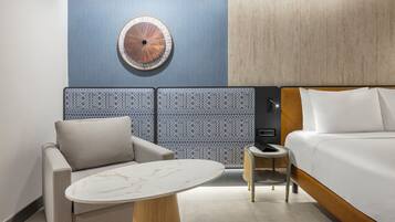 A hotel room with a bed, a round wall decoration, a patterned wall, a sofa, a small round table, and a nightstand.