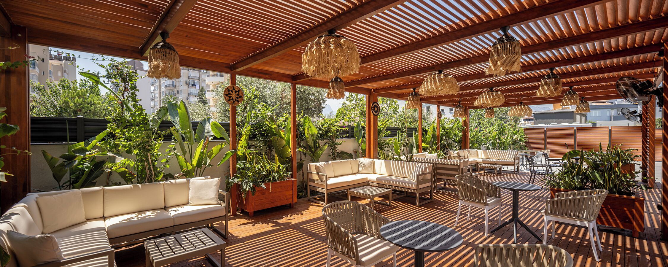 A covered outdoor seating area with wooden furniture, hanging lamps, and potted plants.