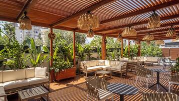 A covered outdoor seating area with wooden furniture, hanging lamps, and potted plants.