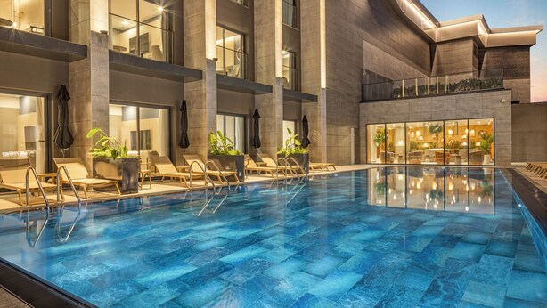 Une piscine intérieure moderne, avec une eau d’un bleu limpide, entourée de chaises longues et de plantes en pot.