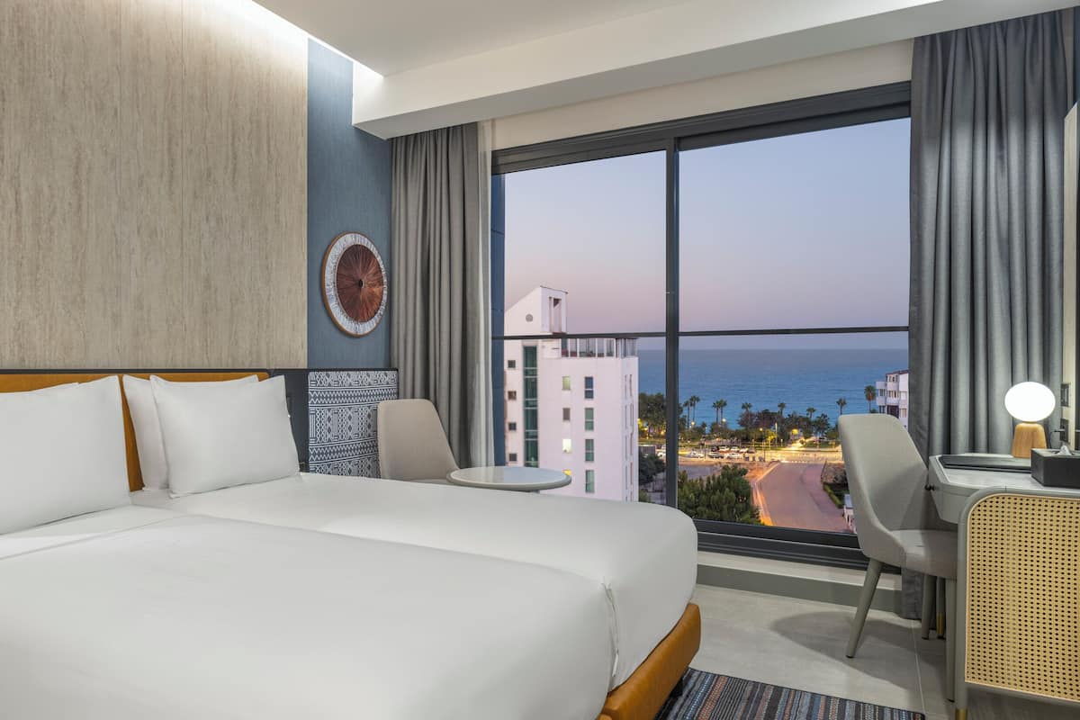 Habitación de hotel con una cama grande, un escritorio con silla, una mesita y vista al océano.