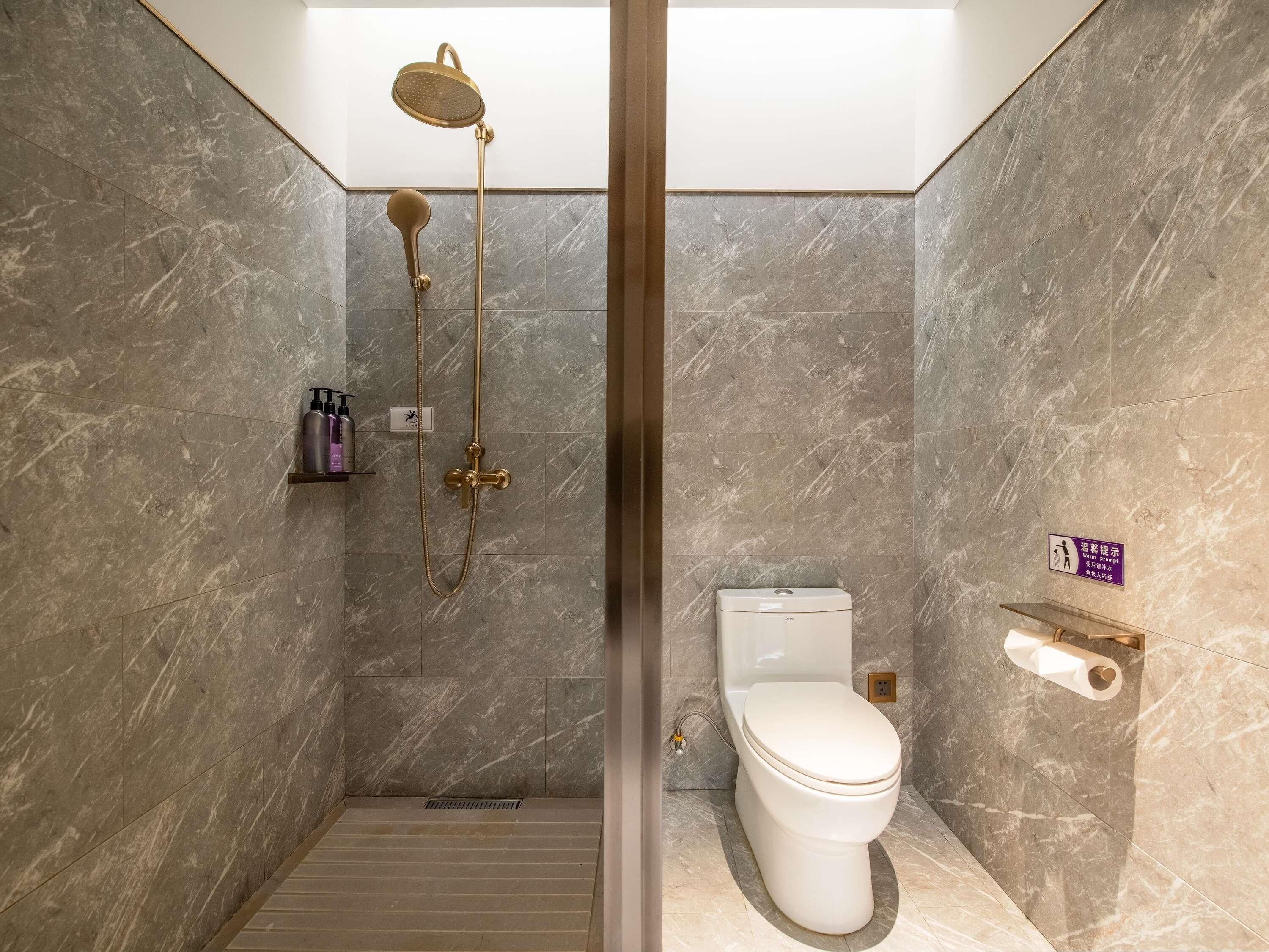 A modern bathroom with a shower, toilet, and marble walls.
