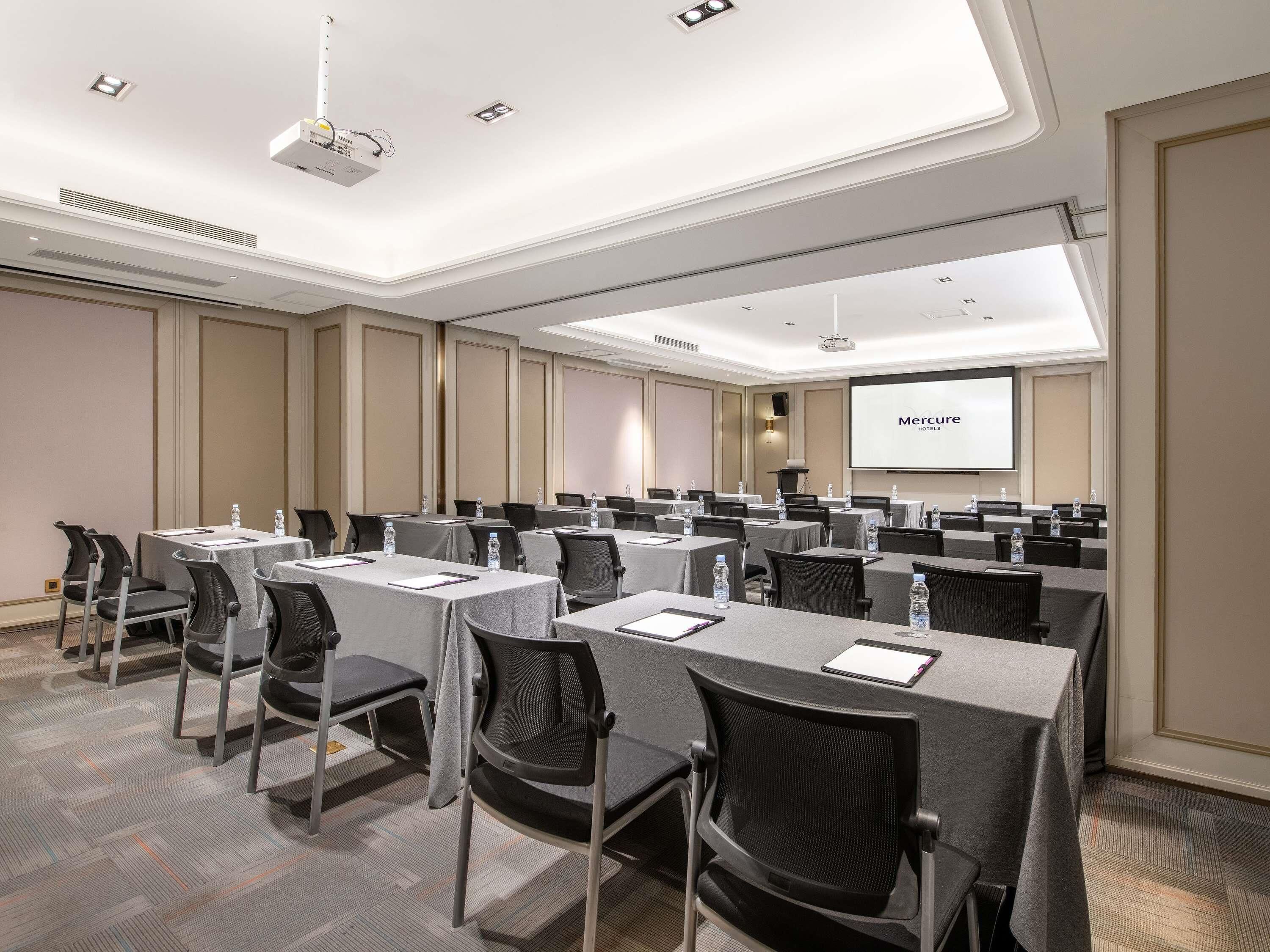A conference room with tables, chairs, a projector, and a screen displaying 'Mercure Hotels'.