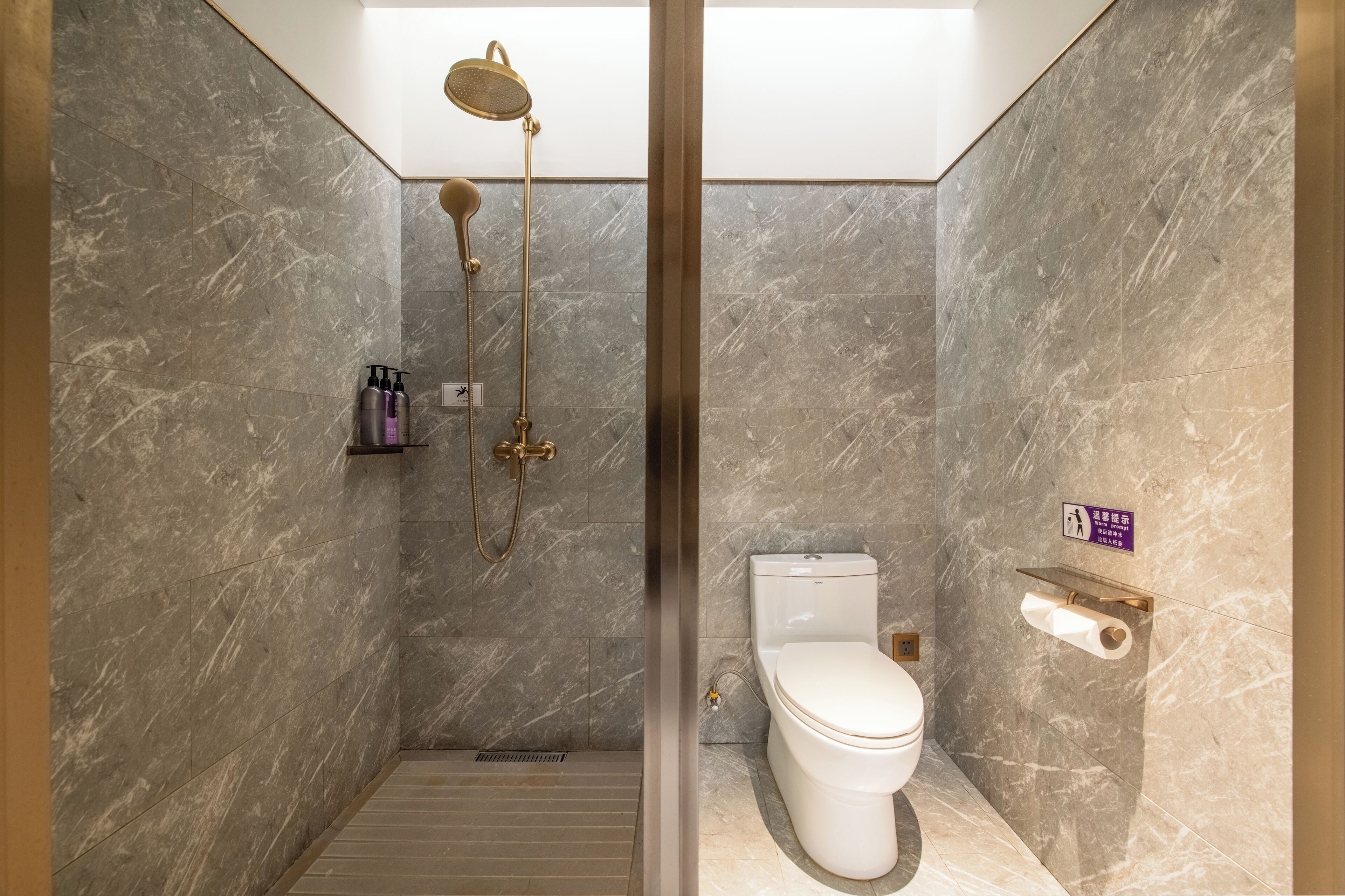 A modern bathroom with a shower, toilet, and marble walls.