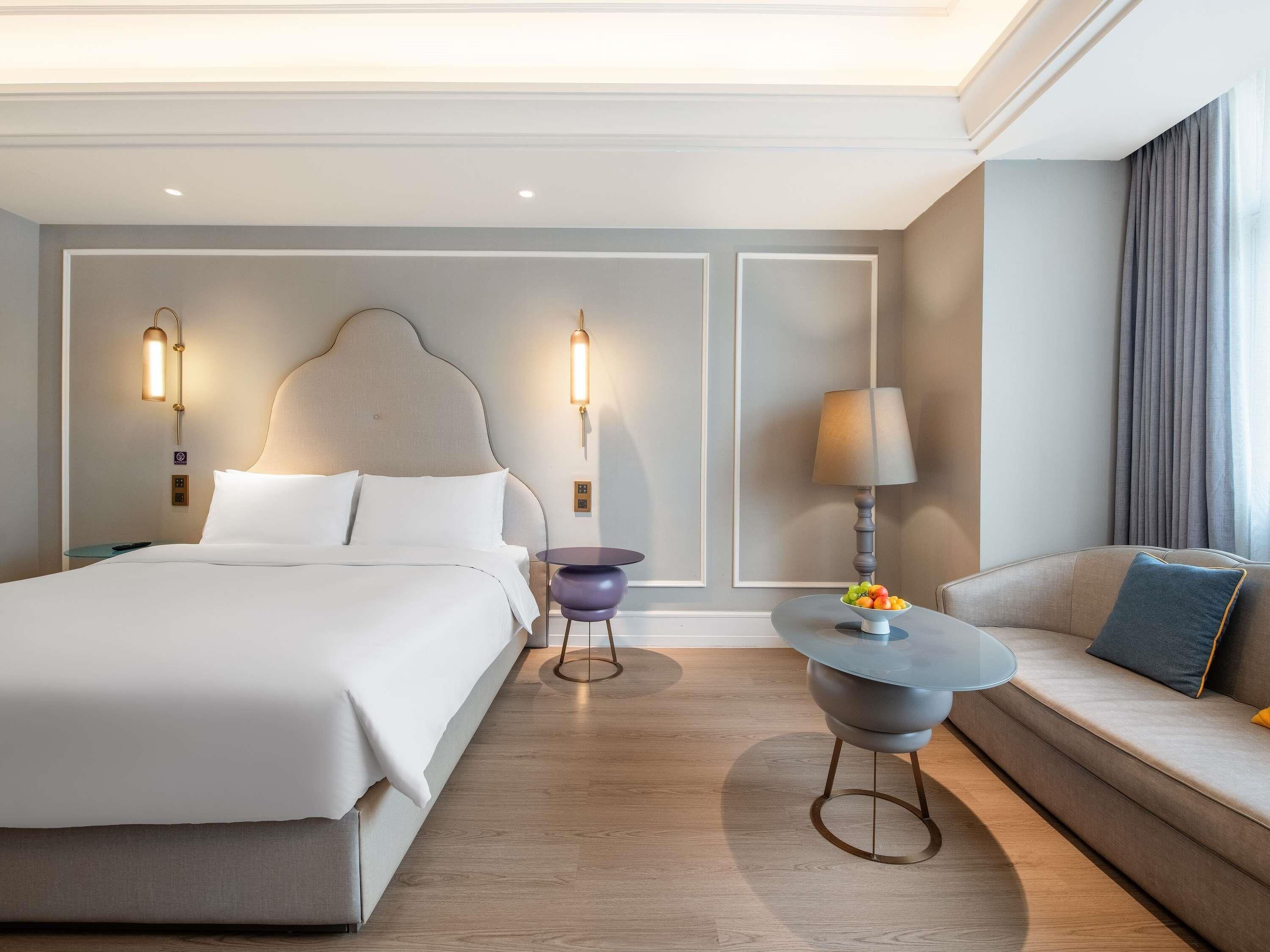 Una habitación de hotel con cama, sofá, una mesa redonda y dos lámparas de pared.