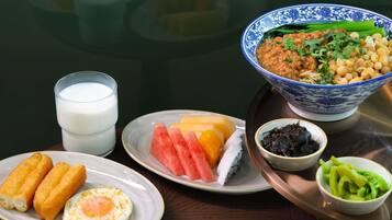 A table with a bowl of soup, a glass of milk, a plate with eggs and corn, a plate with fruit, and a bowl of vegetables.