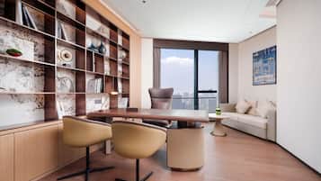 A modern living room with a wooden desk, two chairs, a sofa, and a large window with a city view.