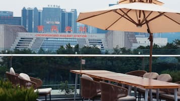 A rooftop terrace with a table and chairs, a large umbrella, and a view of the Chongqing Railway Station in the background.