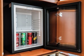 Un petit réfrigérateur doté d’un compartiment congélateur situé à droite, contenant quatre canettes de boissons.