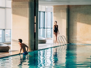 Ein Hallenbad mit klarem Wasser, einem Sprungbrett und großen Fenstern.