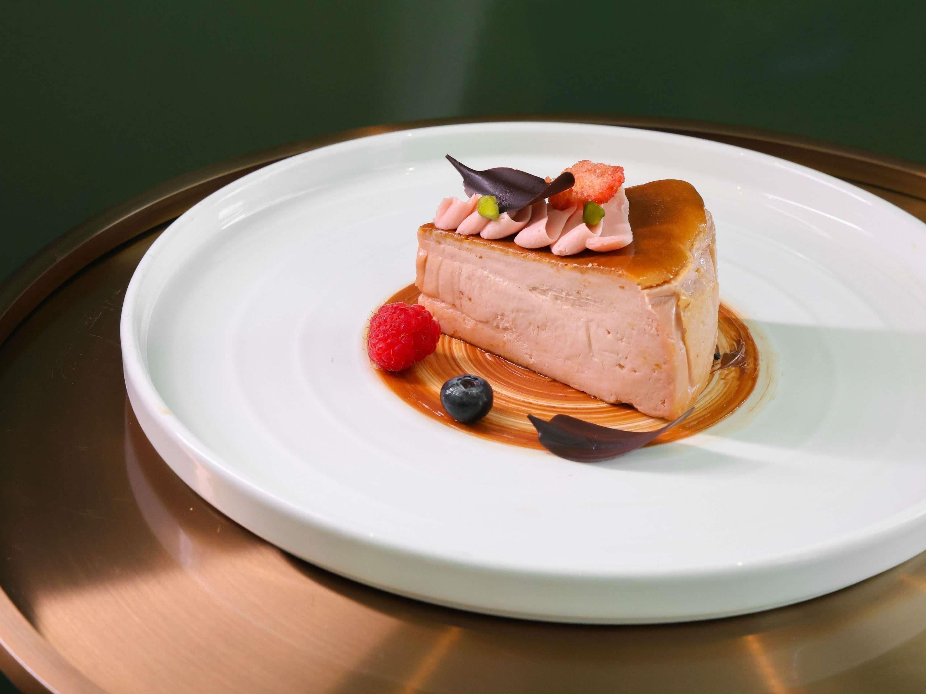 A dessert on a white plate with a caramel sauce, raspberries, and blueberries.
