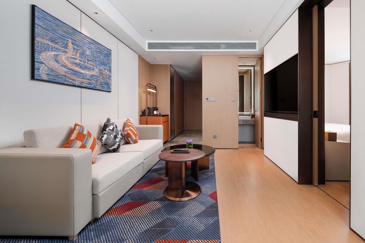 Ein modernes Hotelzimmer mit Sofa, Couchtisch, Gemälde, Spiegel und Fernseher.