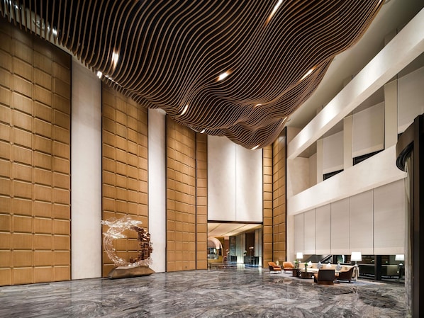Eine großzügige Lobby mit hoher Decke, holzverkleideten Wänden, einem Marmorboden und einer Sitzecke mit Tischen und Stühlen.