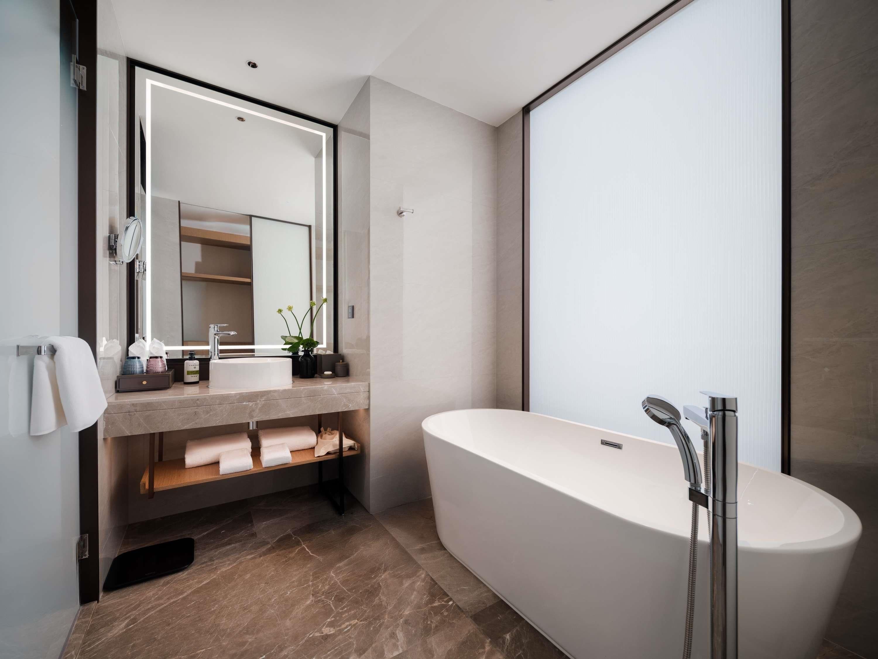 A modern bathroom with a freestanding bathtub, a large mirror, and a vanity with a sink and towel rack.