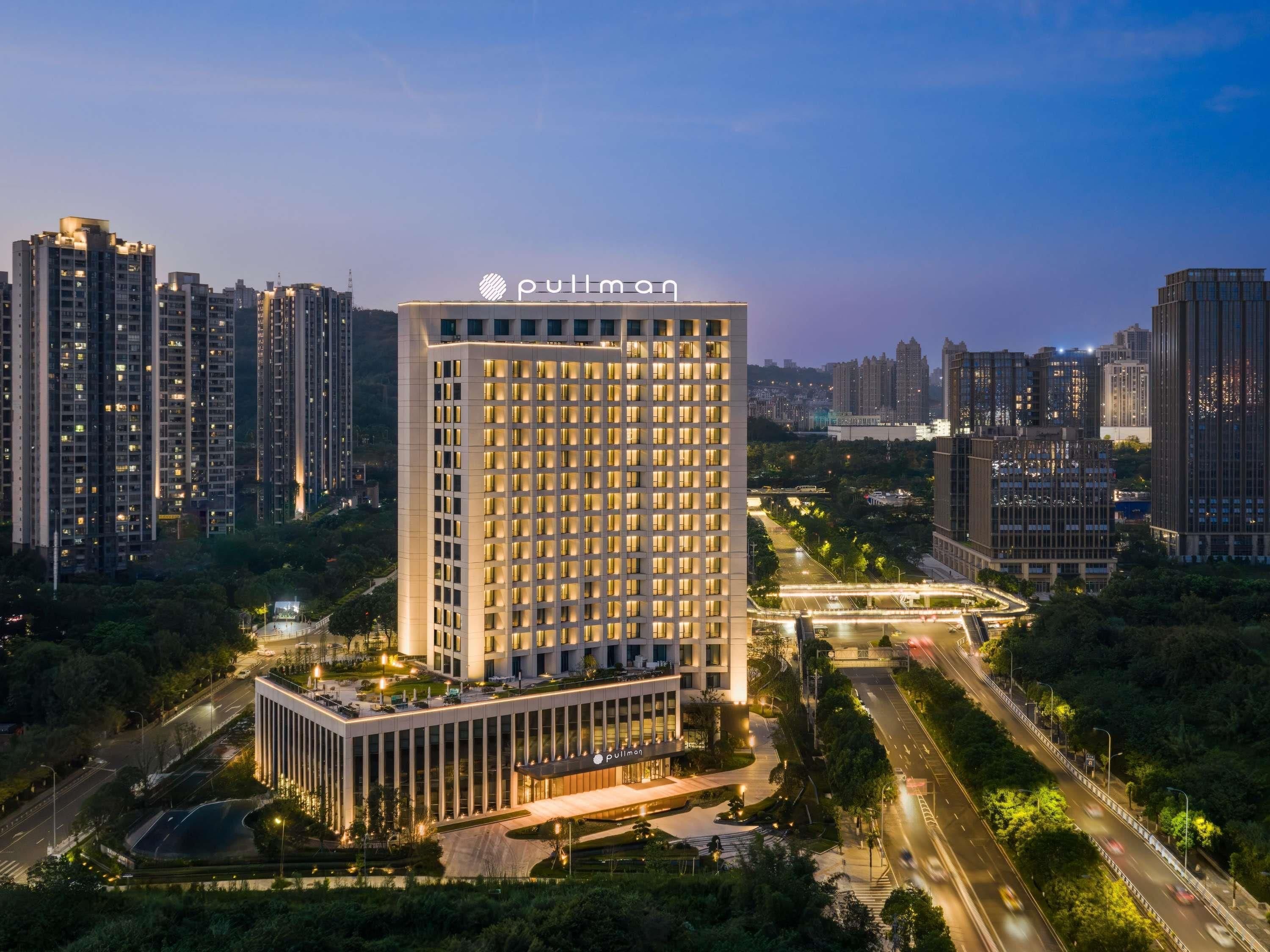 A high-rise building with a prominent 'pullman' sign, surrounded by other high-rise buildings and a well-lit urban environment.
