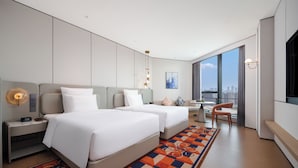 Une chambre d’hôtel moderne avec deux lits, un bureau et une grande fenêtre donnant sur la ville.