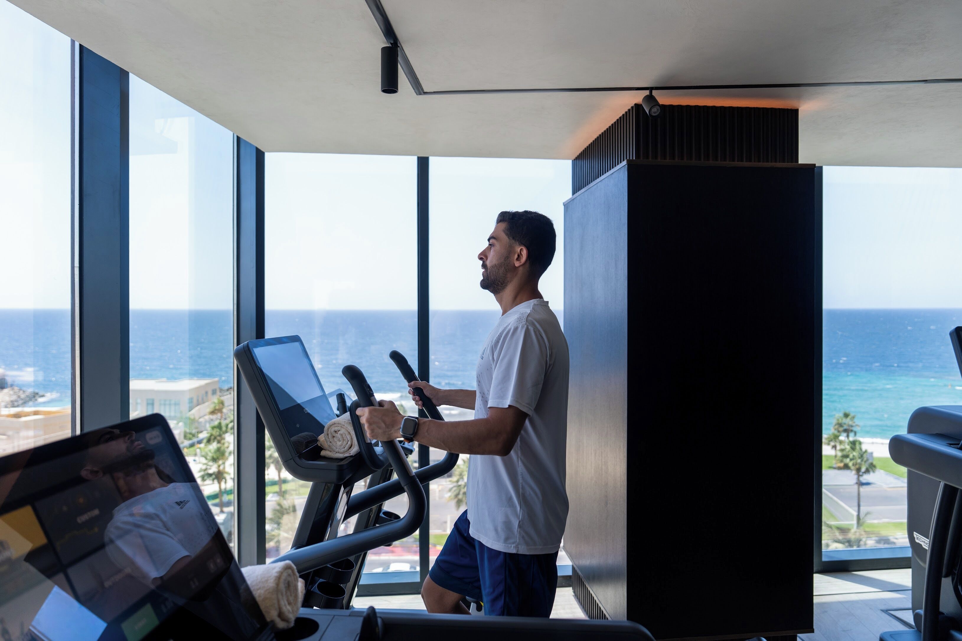 A man using an exercise machine in a room with large windows overlooking the ocean.