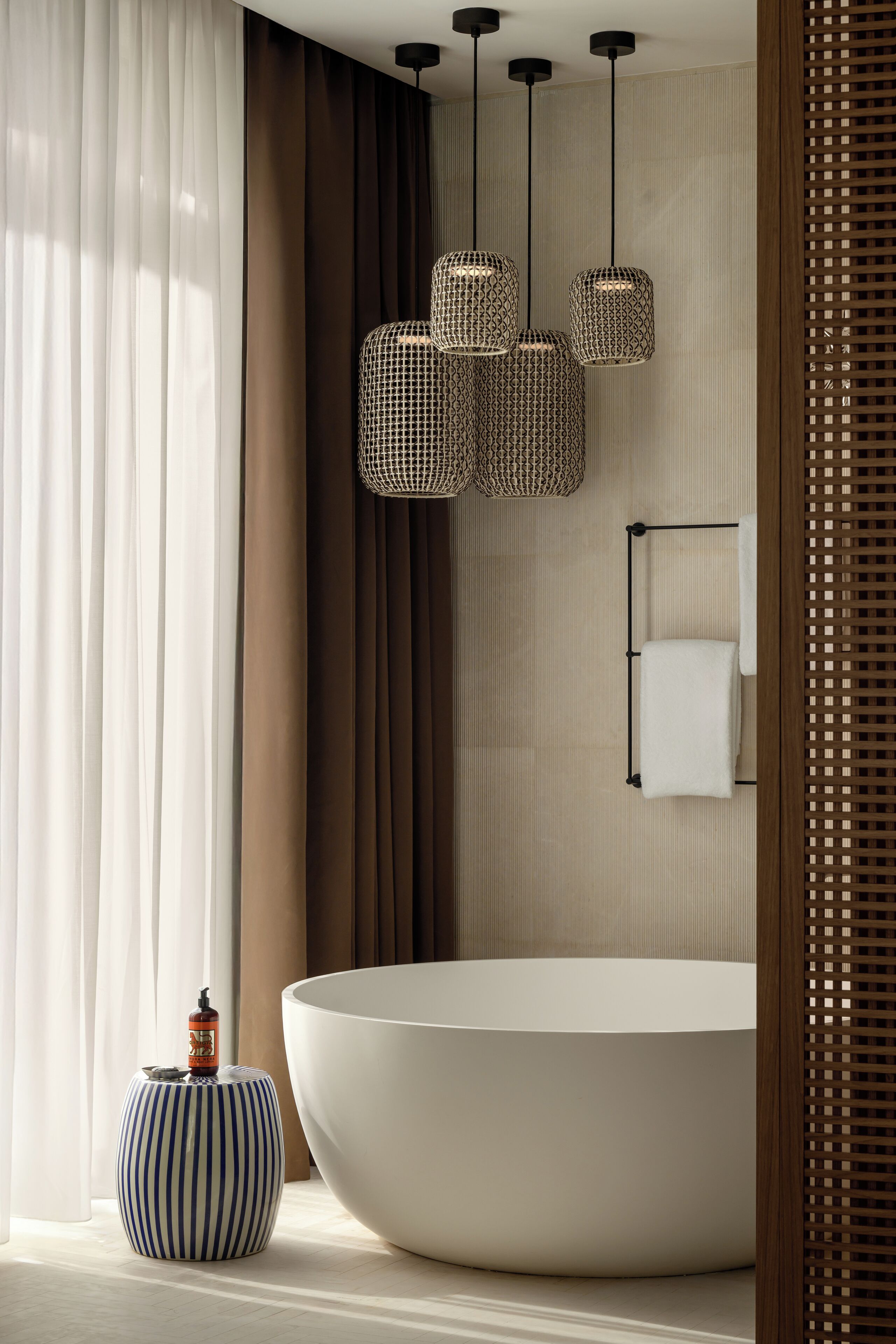 A modern bathroom with a large bathtub, a striped stool, and a bottle of shampoo.