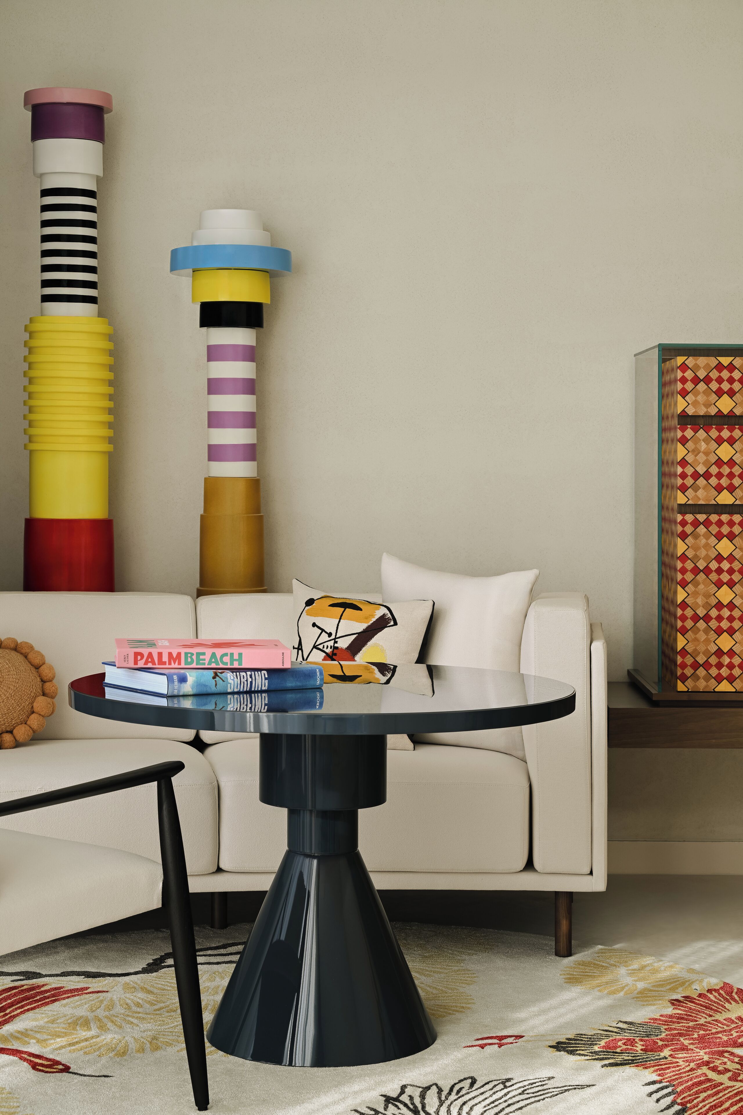 A modern living room with a round black table, a white sofa, and a colorful abstract painting.