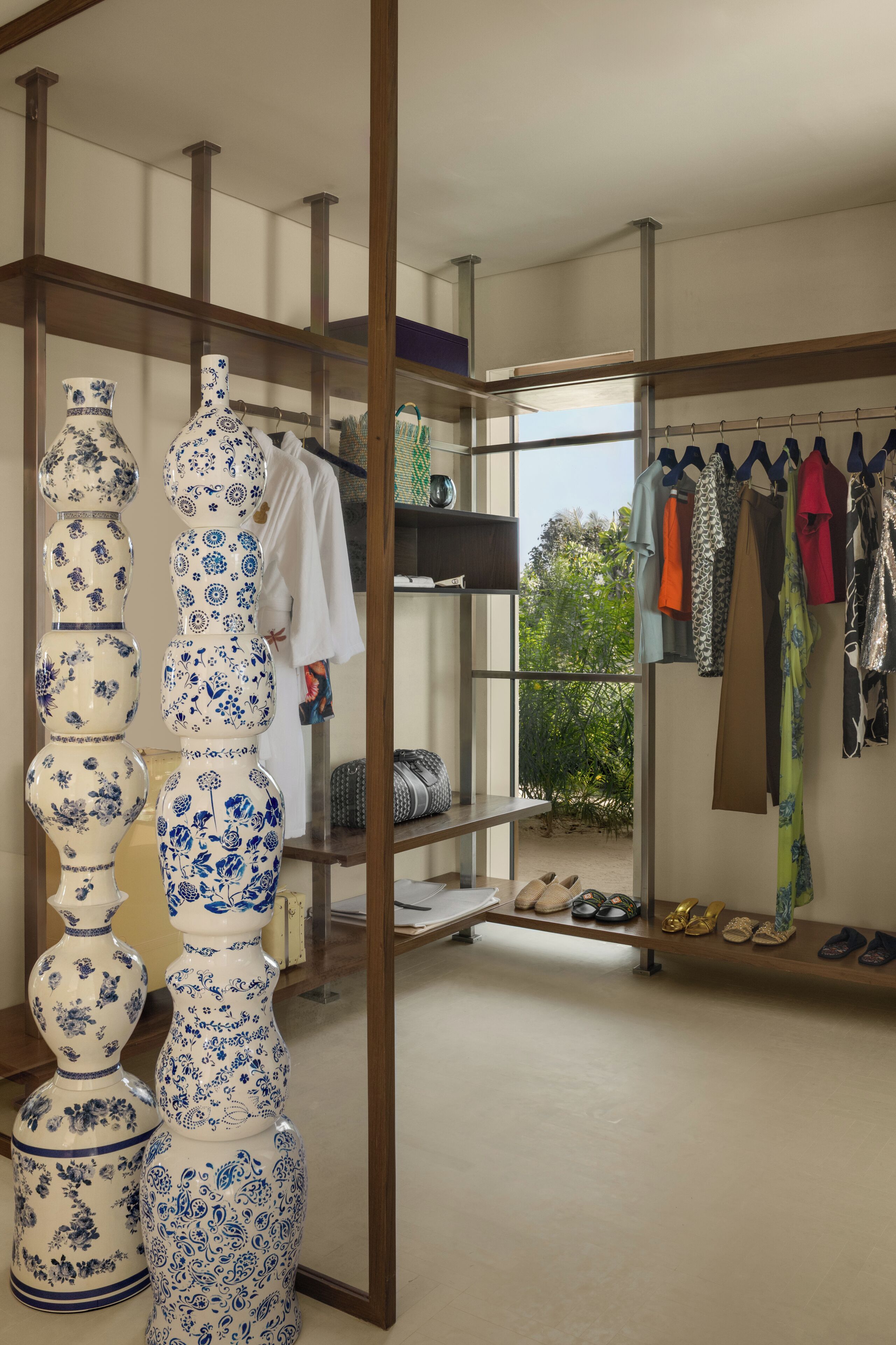 Een kamer met een presentatie van blauwe en witte vazen, een kledingrek met verschillende kledingstukken en een schoenenrek met meerdere paar schoenen.