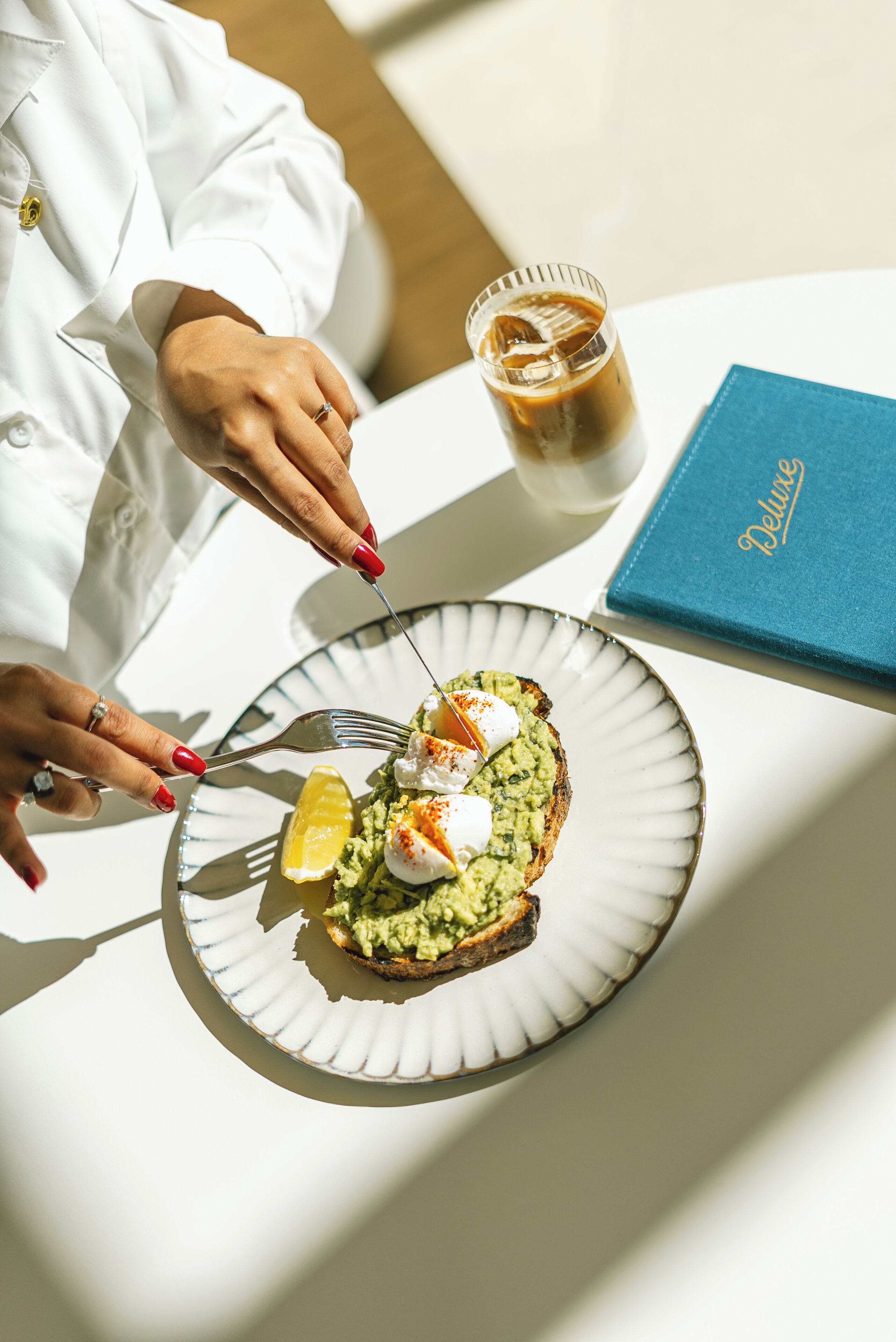 Une personne est assise à une table devant une assiette de nourriture, un verre de café glacé et un menu bleu.
