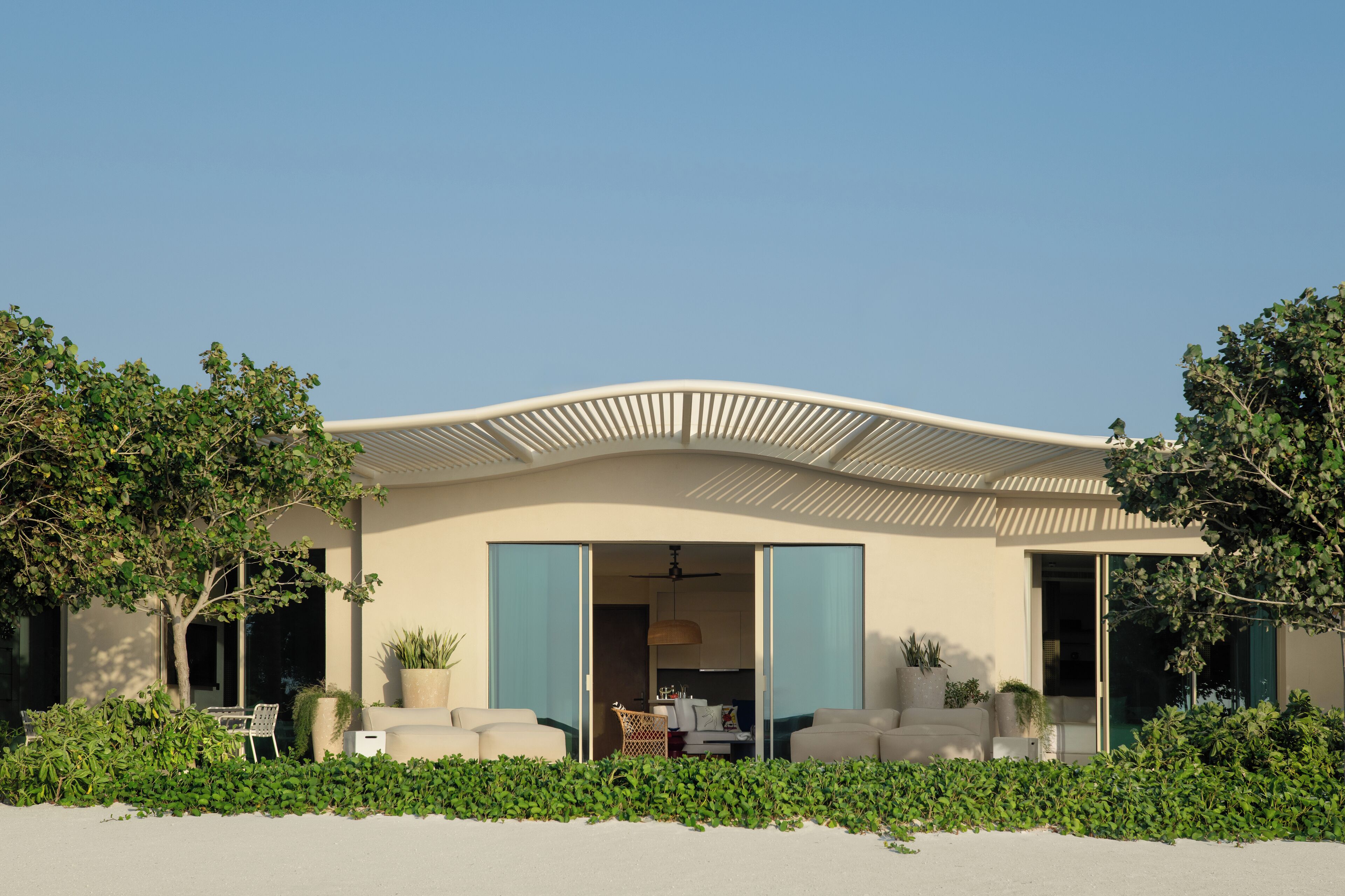 Una casa moderna con techo curvo, un patio con mobiliario exterior y vista al interior a través de puertas abiertas.