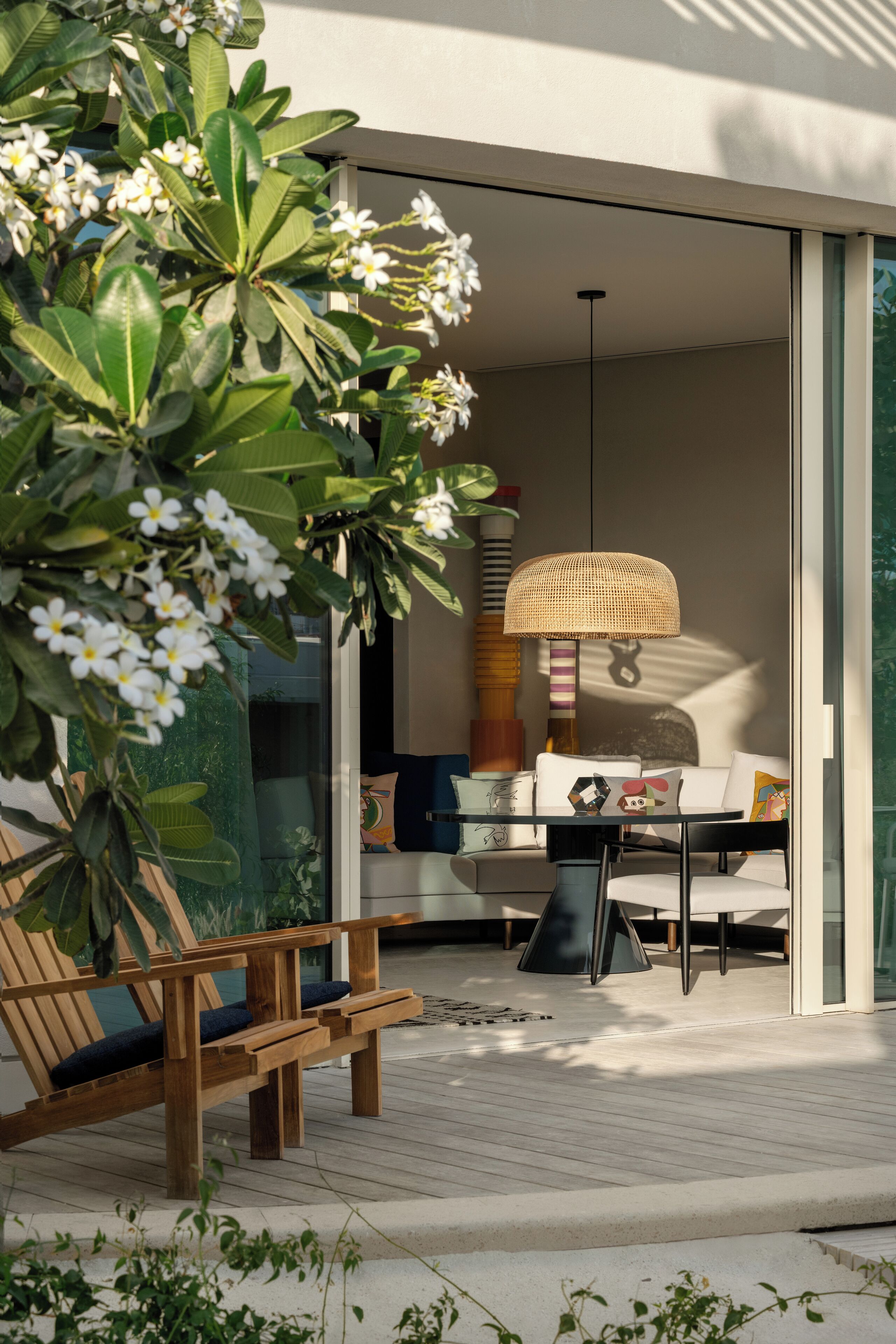 Un'area relax esterna moderna con una panchina in legno e un tavolo, immersa nel verde e circondata da fiori bianchi.