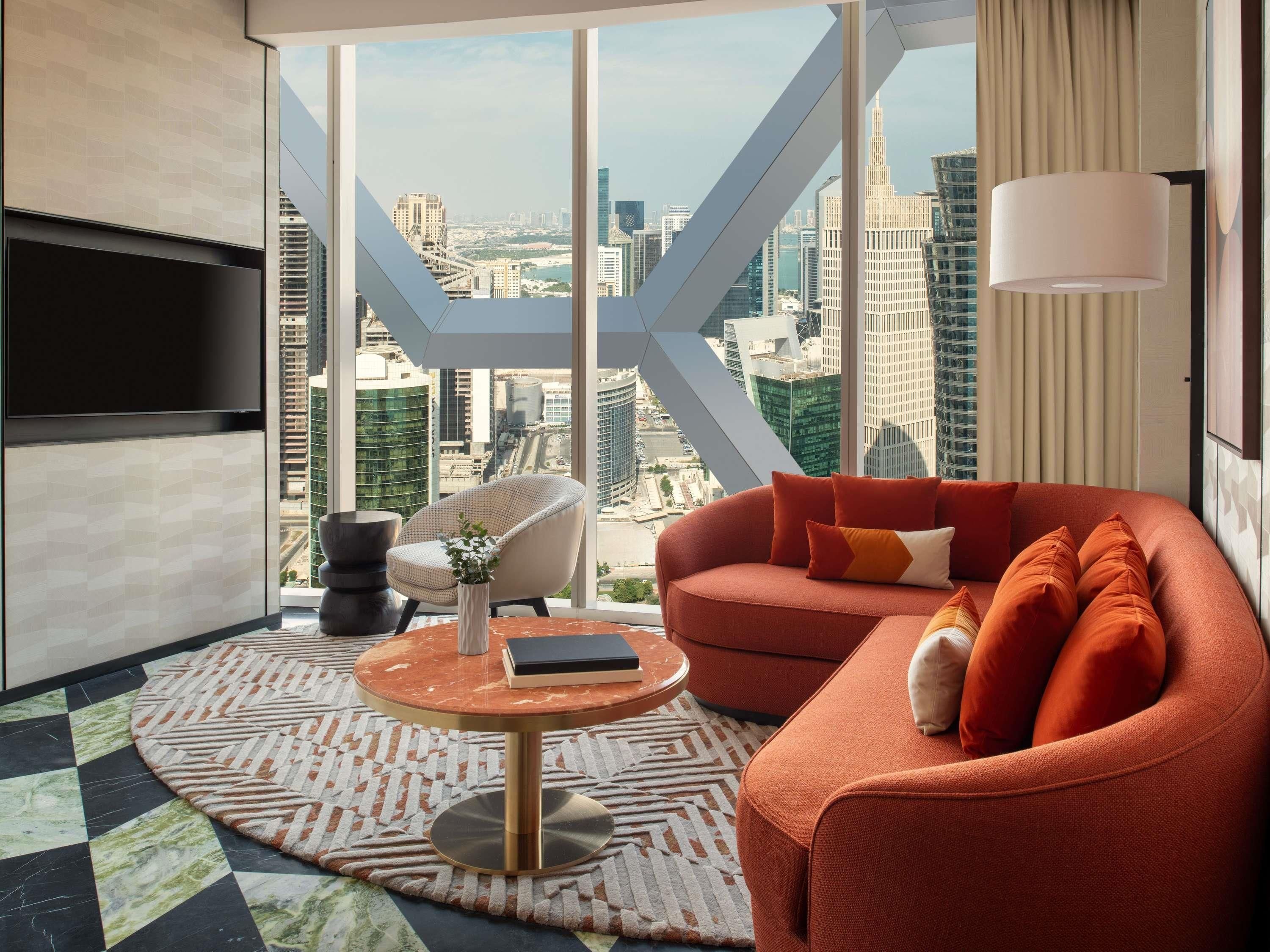 Ein modernes Wohnzimmer mit einer Couch, einem runden Couchtisch und einem Sessel, mit Blick auf die Stadt durch große Fenster.