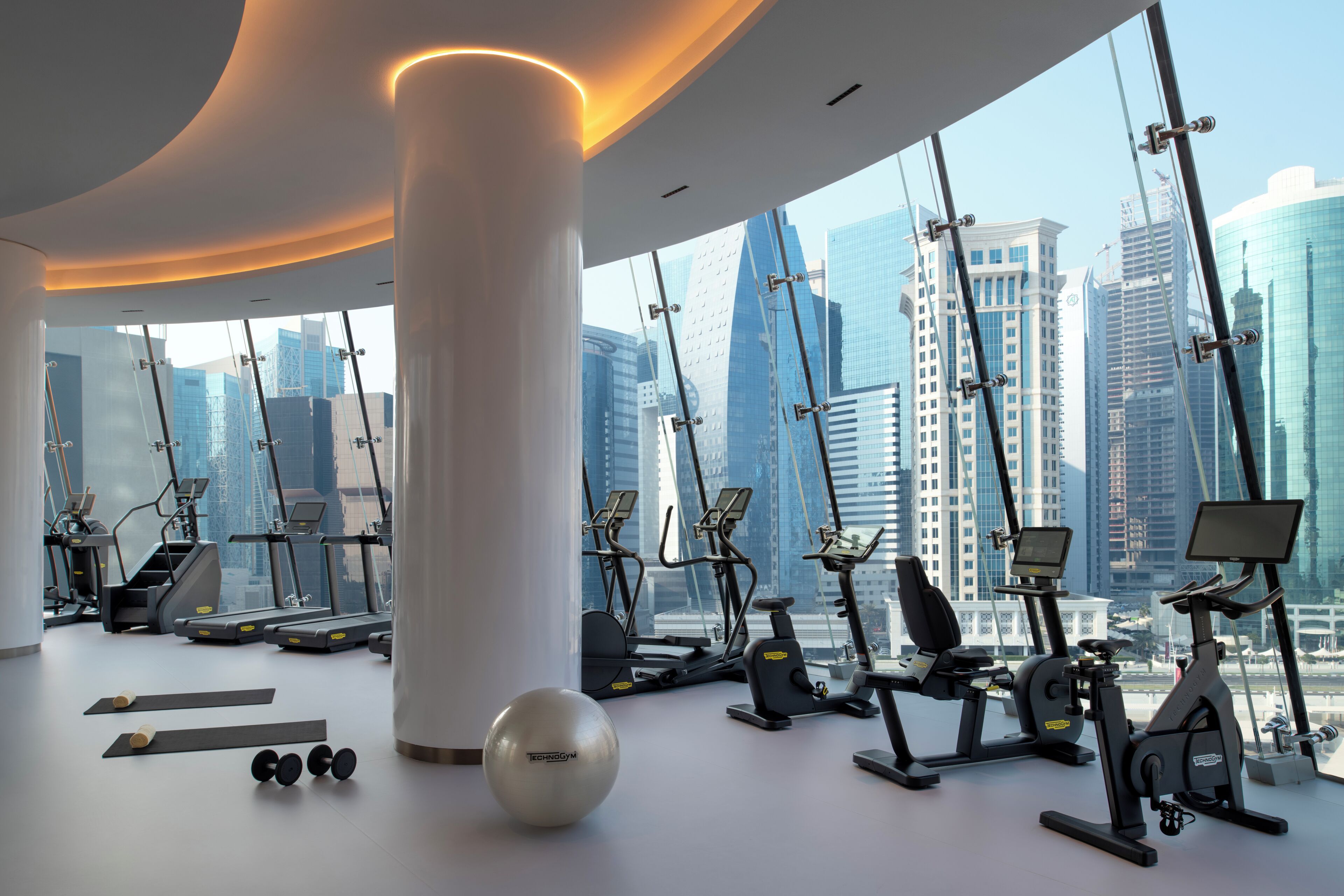 A modern gym with various exercise equipment and a large window offering a city view.