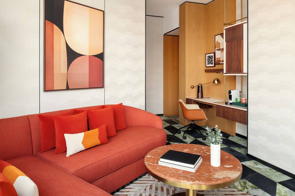 Una sala de estar moderna con un sofá rojo, una mesita redonda con un libro y un jarrón, y un escritorio con una silla.