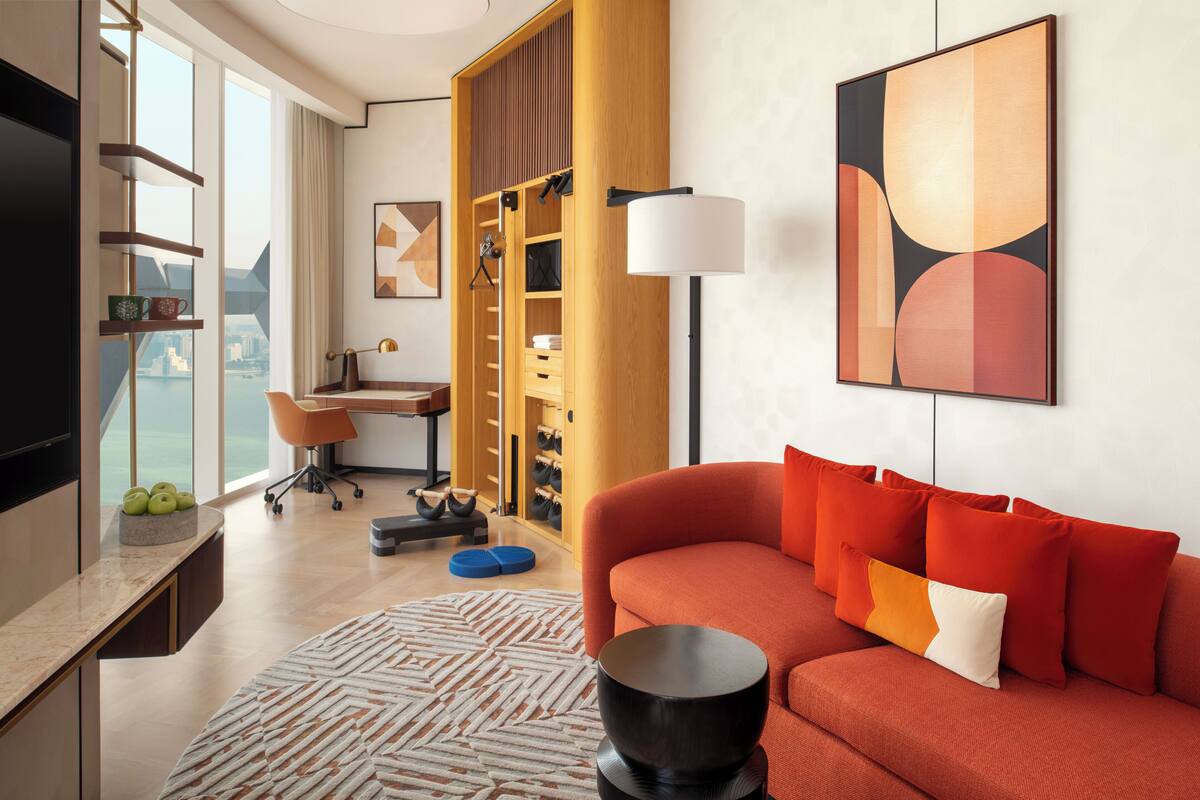 Una habitación de hotel moderna con un ventanal grande, un sofá, un escritorio y un armario.