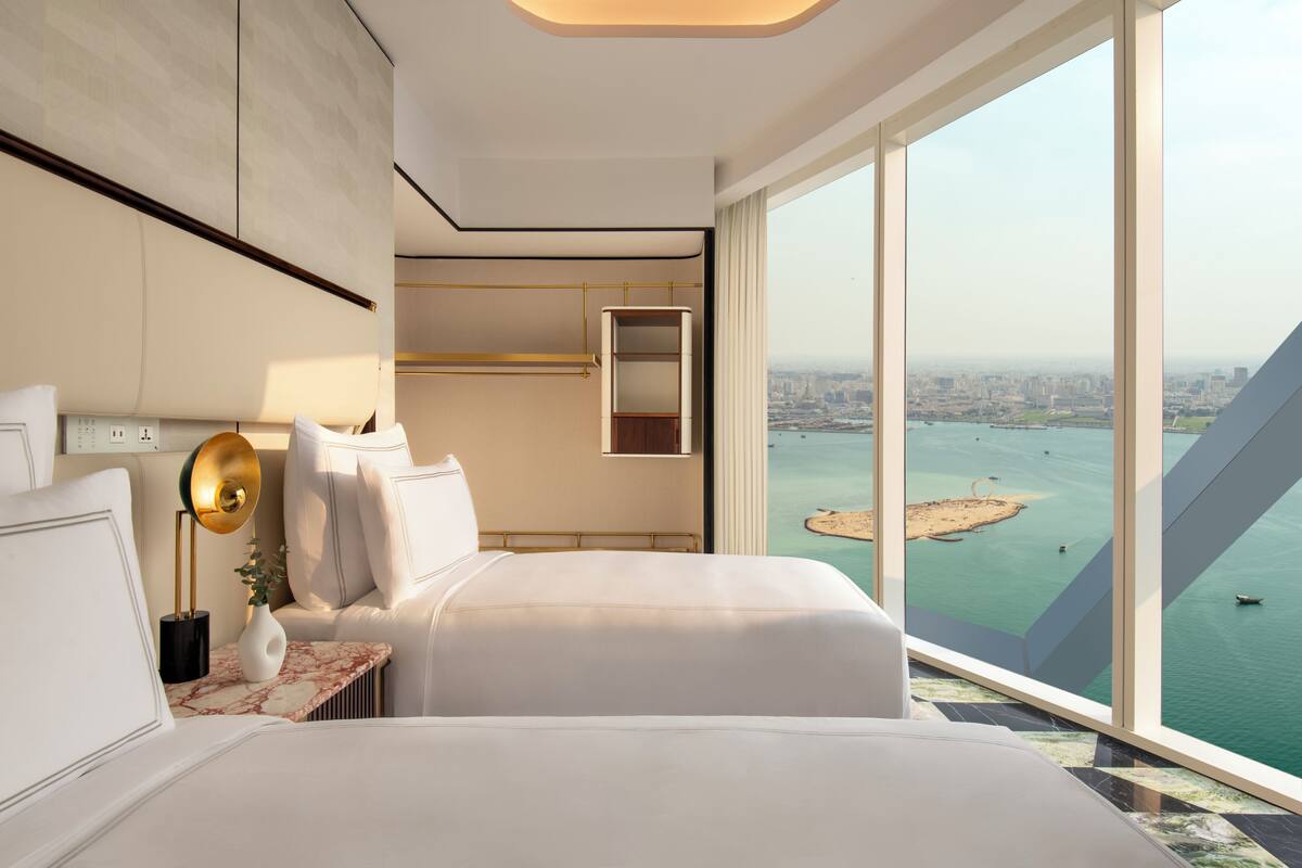 Una habitación de hotel moderna con una cama grande, una mesita de noche, un espejo y vistas a la ciudad y al agua.